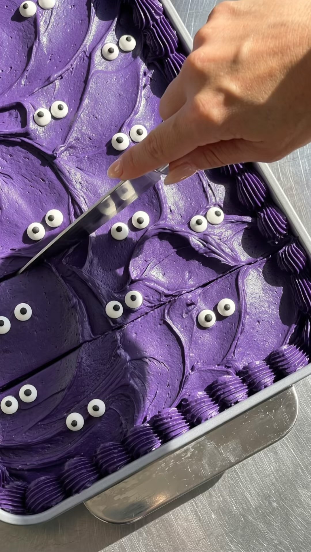 Top view of slicing a Halloween cake with purple ube frosting into squares in a baking pan by Ube Nolia