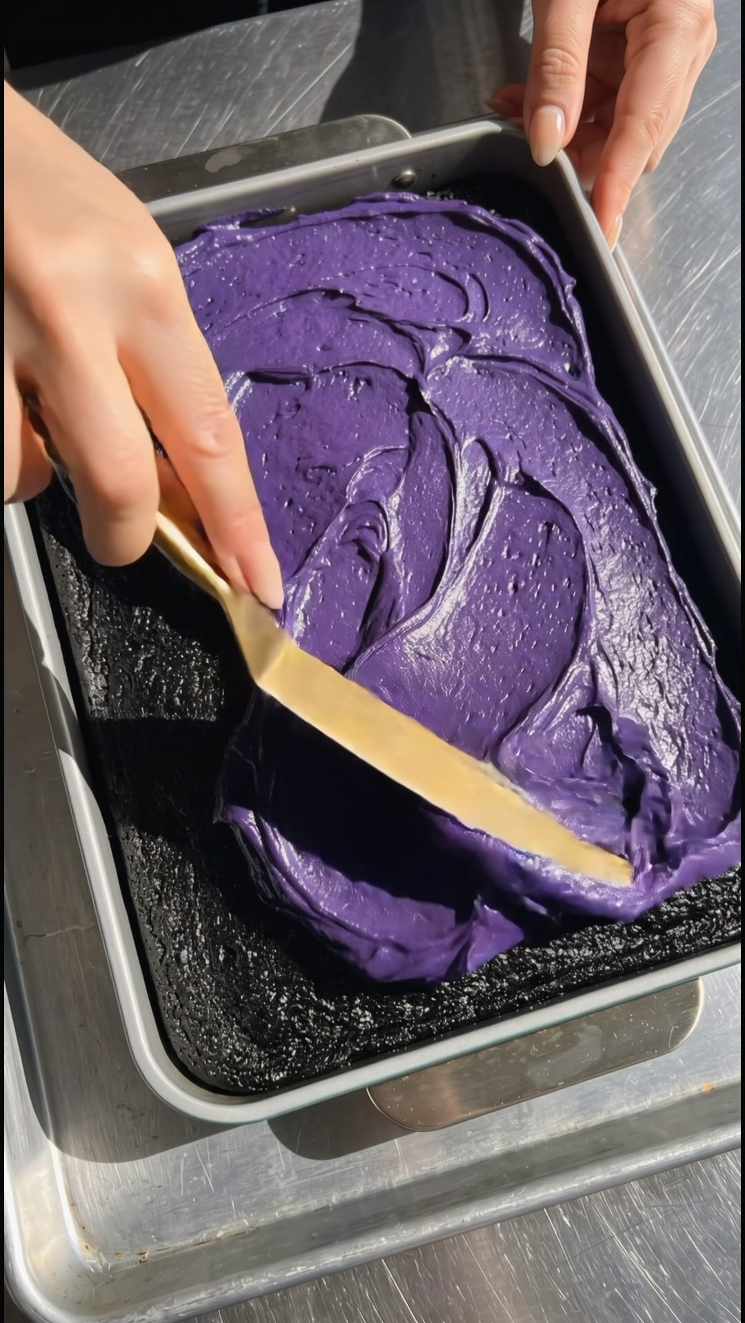 Spreading purple ube frosting with an offset spatula over a black velvet cake in a baking dish by Ube Nolia