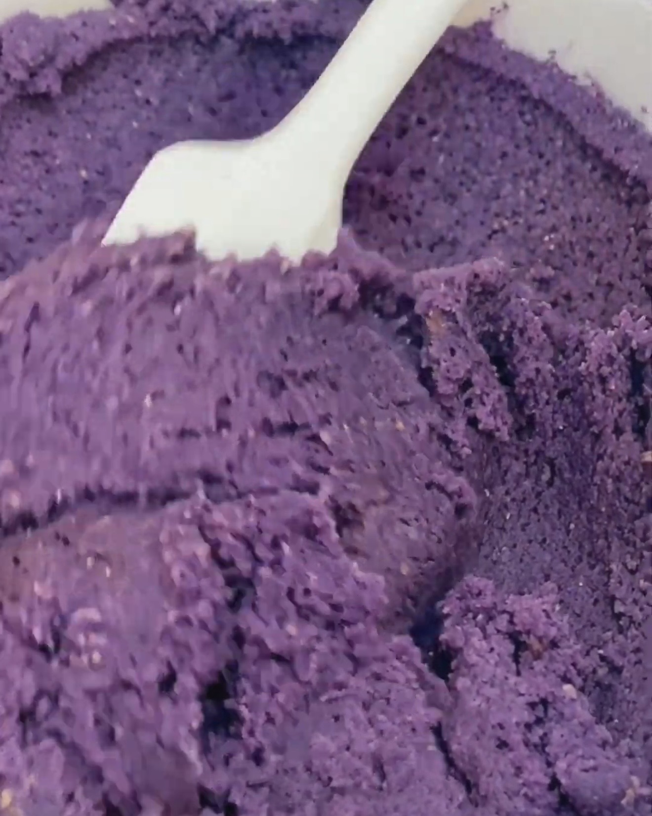 Massa de biscoito de ube roxo profundo a ser envolvida com uma espátula branca depois de adicionar ube powder UBE NOLIA®