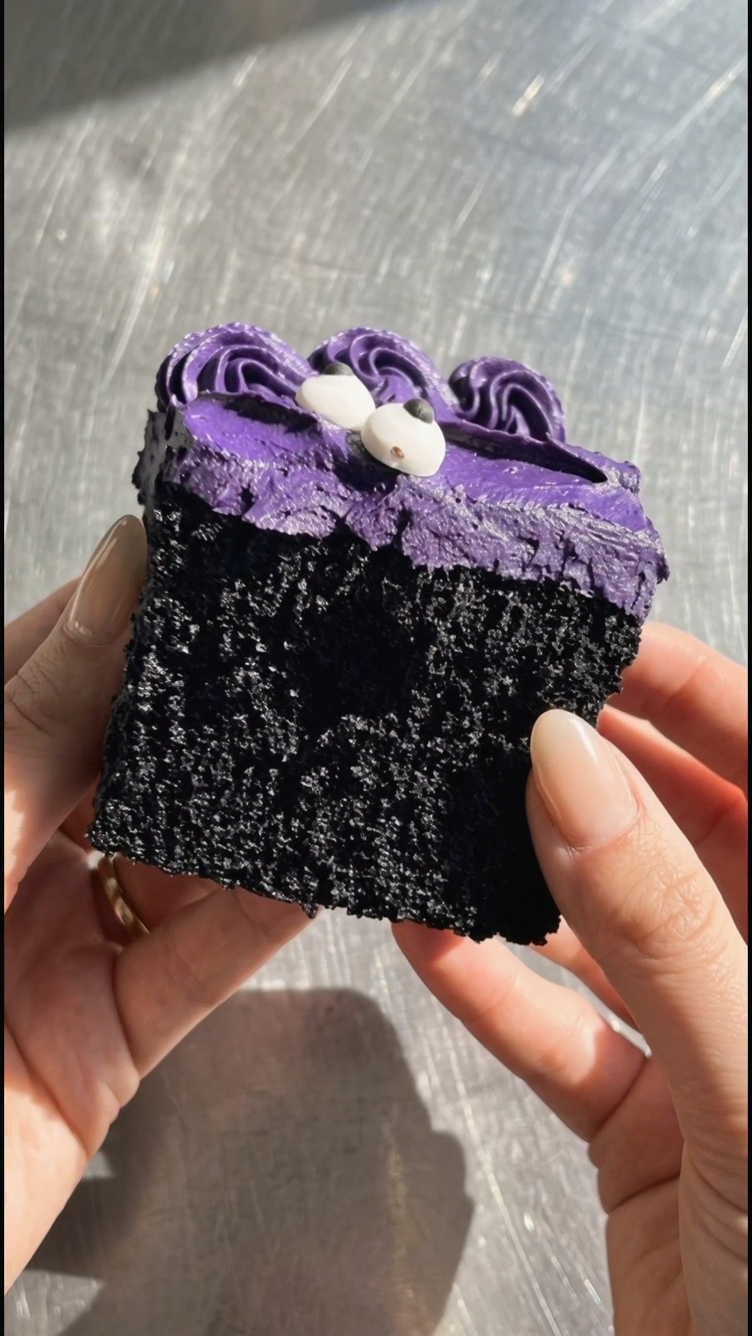 Hand holding a slice of Halloween cake showing the tender black crumb and thick purple ube frosting by Ube Nolia