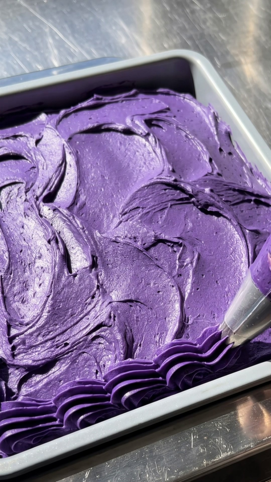 Piping a purple ube frosting border with a star tip onto a black Halloween cake by Ube Nolia
