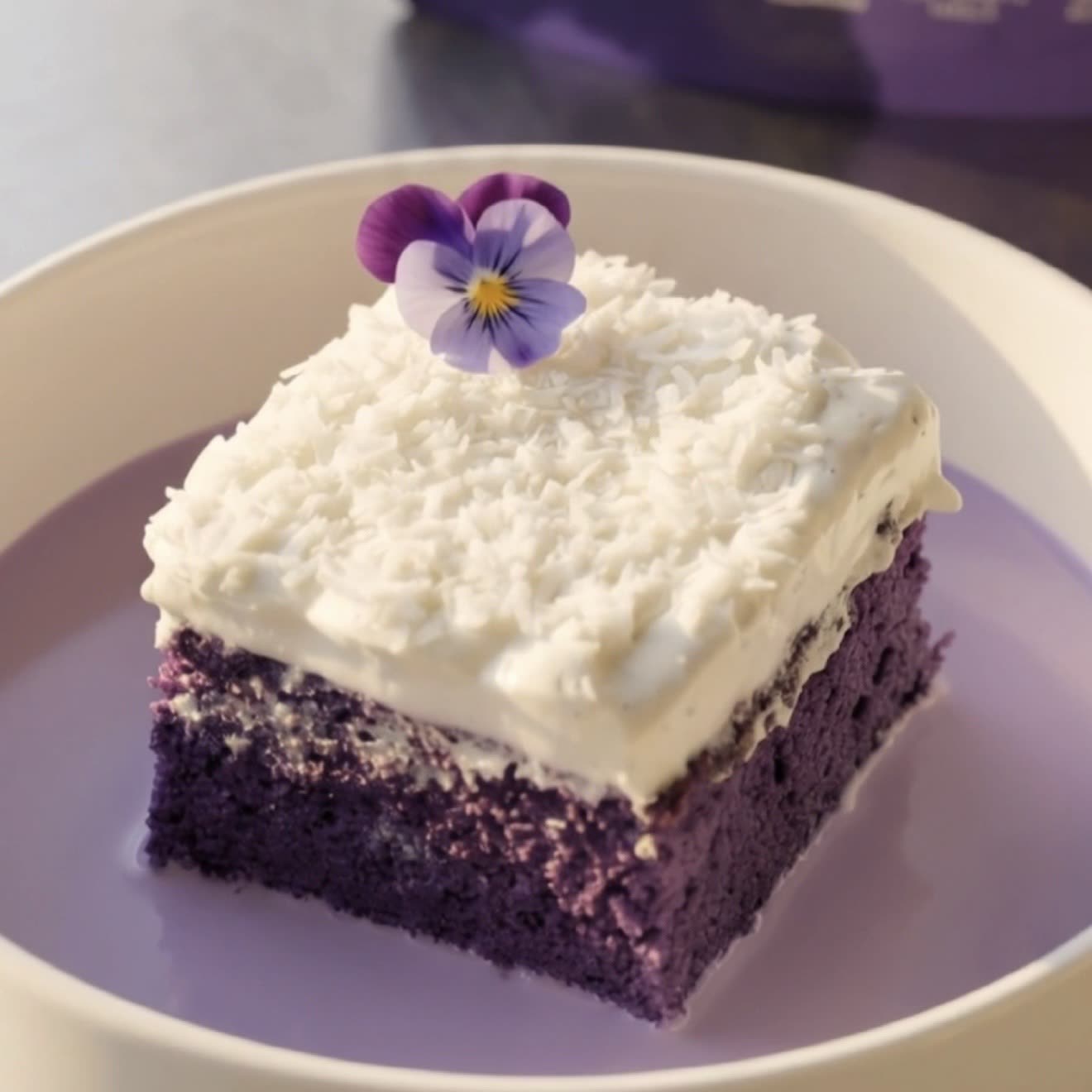 Fetta di torta tres leches all'ube e cocco con panna montata al cocco e cocco grattugiato, pronta da servire | Ube Nolia