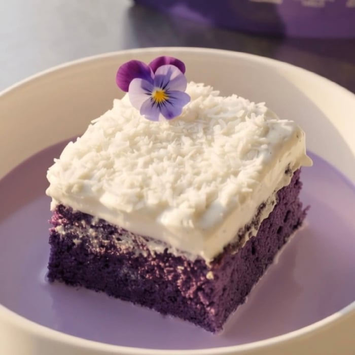 Slice of ube coconut tres leches cake topped with coconut whipped cream and shredded coconut, ready to serve | Ube Nolia