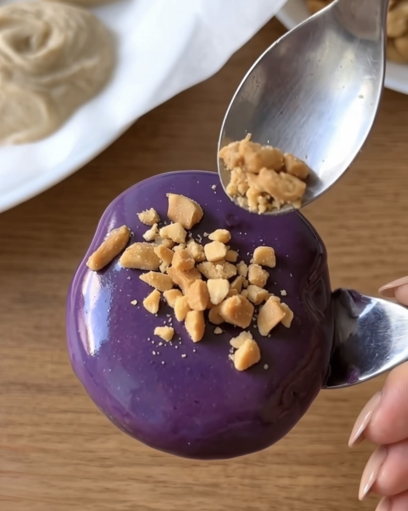 Cacahuetes tostados triturados espolvoreados sobre un bocadito de yogur congelado de UBE NOLIA cubierto de chocolate blanco de ube morado