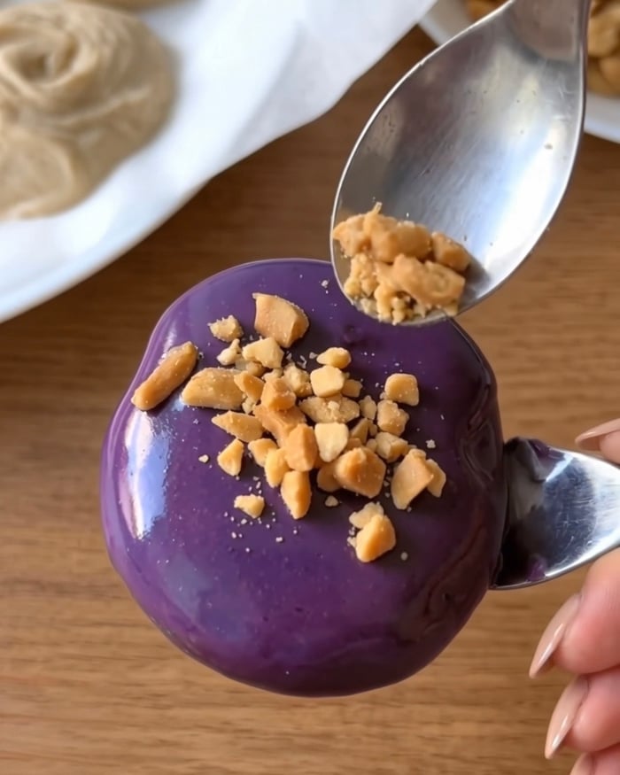 Crushed roasted peanuts sprinkled on a purple ube white chocolate coated Ube Nolia frozen yogurt bite