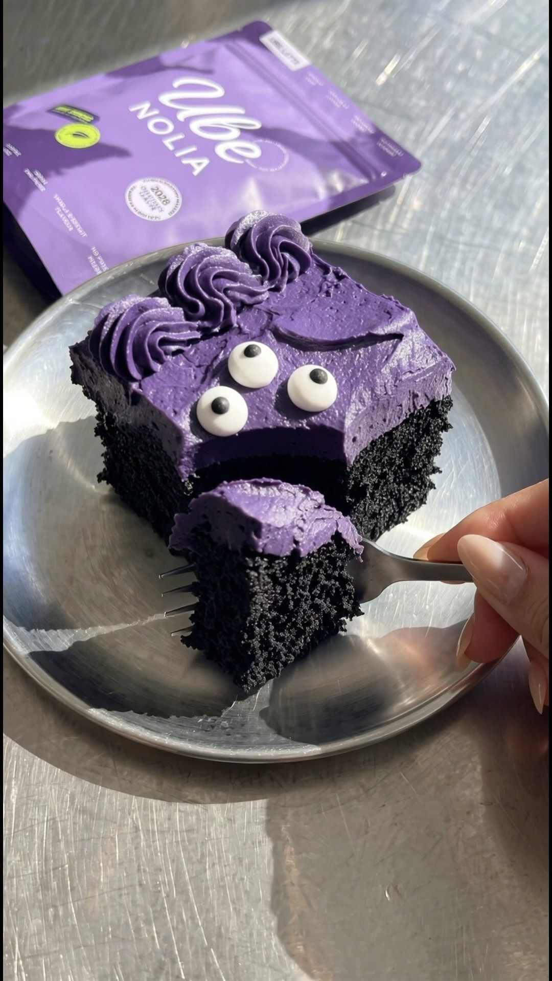 Plated slice of Halloween cake with a bite on a fork and an Ube Nolia package in the background