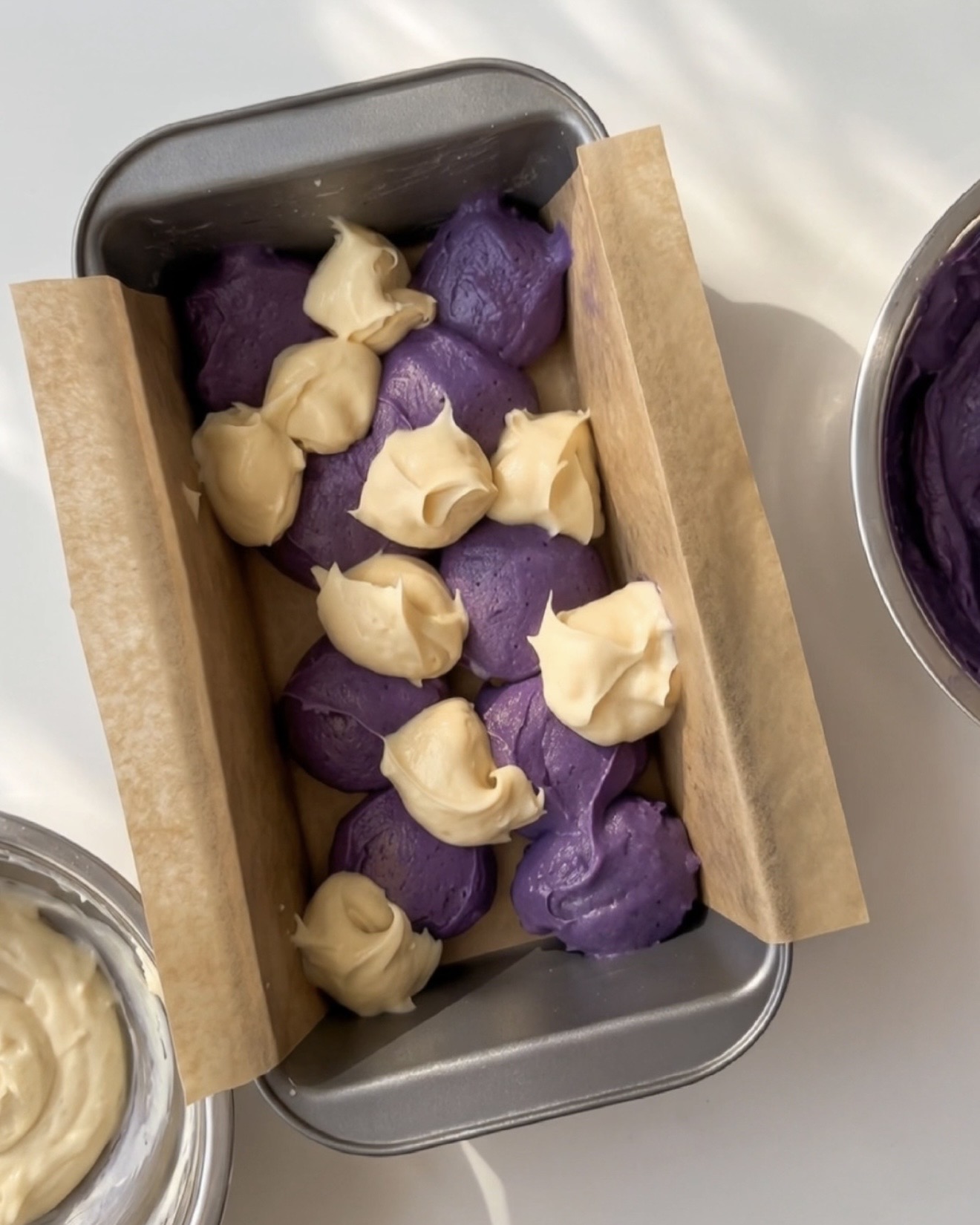 Scoops of purple ube batter and vanilla batter alternated in a lined loaf pan for Ube Nolia ube marble pound cake