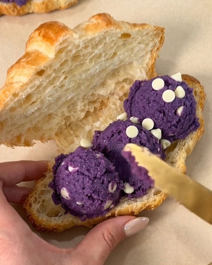 Sprider Ube Nolia lila ube (purple yam) vit chokladbit kakdeg i skedar inuti en skivad smörbakad bagericroissant för att göra en ube crookie