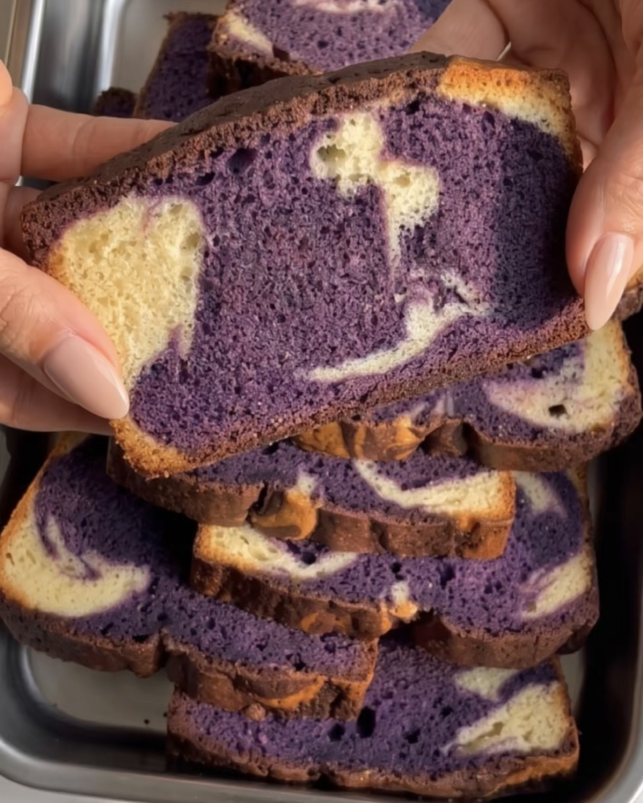 Hand holding a slice of ube marble pound cake with a purple and vanilla swirl, baked with Ube Nolia ube powder