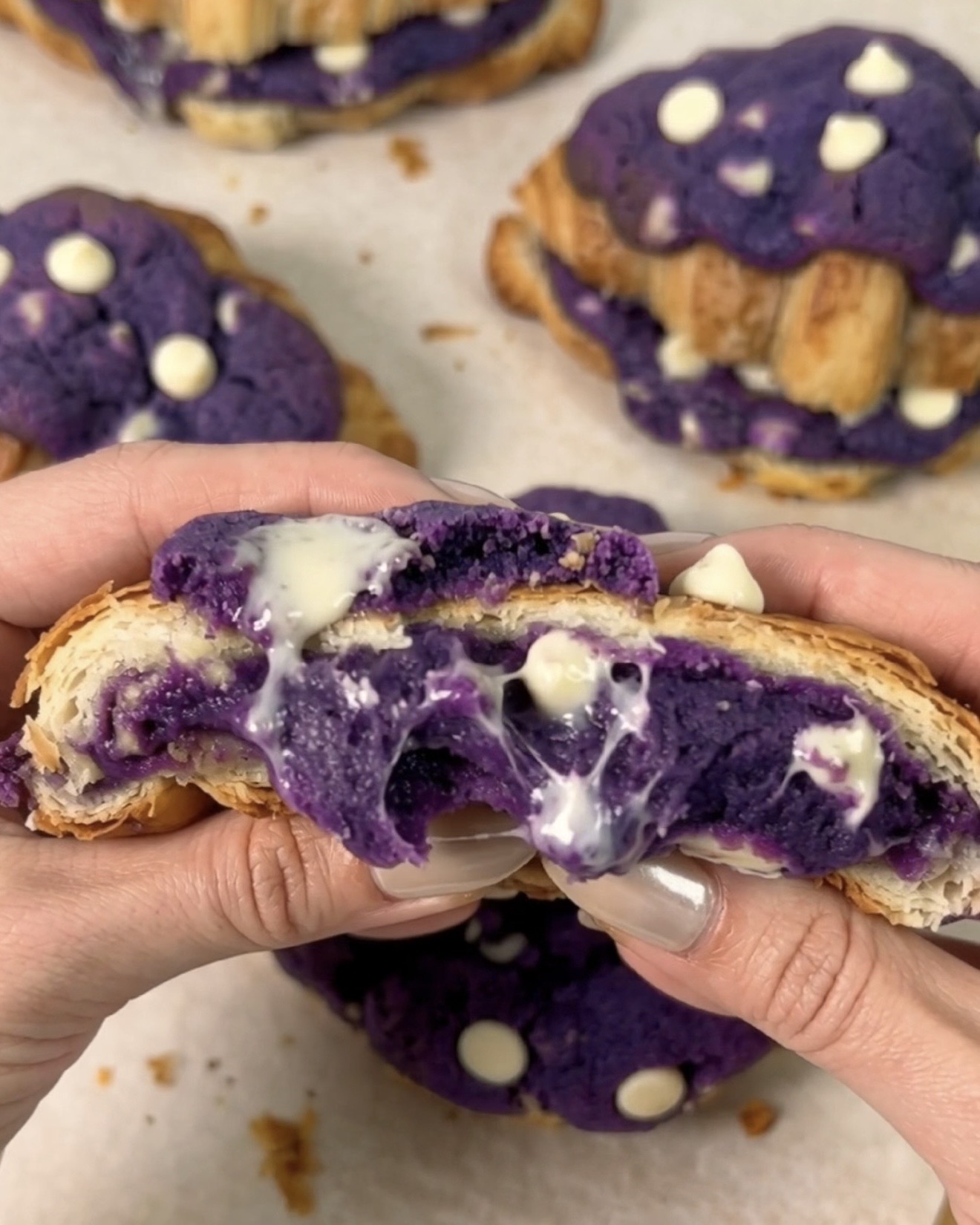 Ube crookies UBE NOLIA® recém-assados, abertos para revelar um centro de biscoito de ube roxo (inhame roxo) com chocolate branco derretido a escorrer entre camadas douradas de croissant