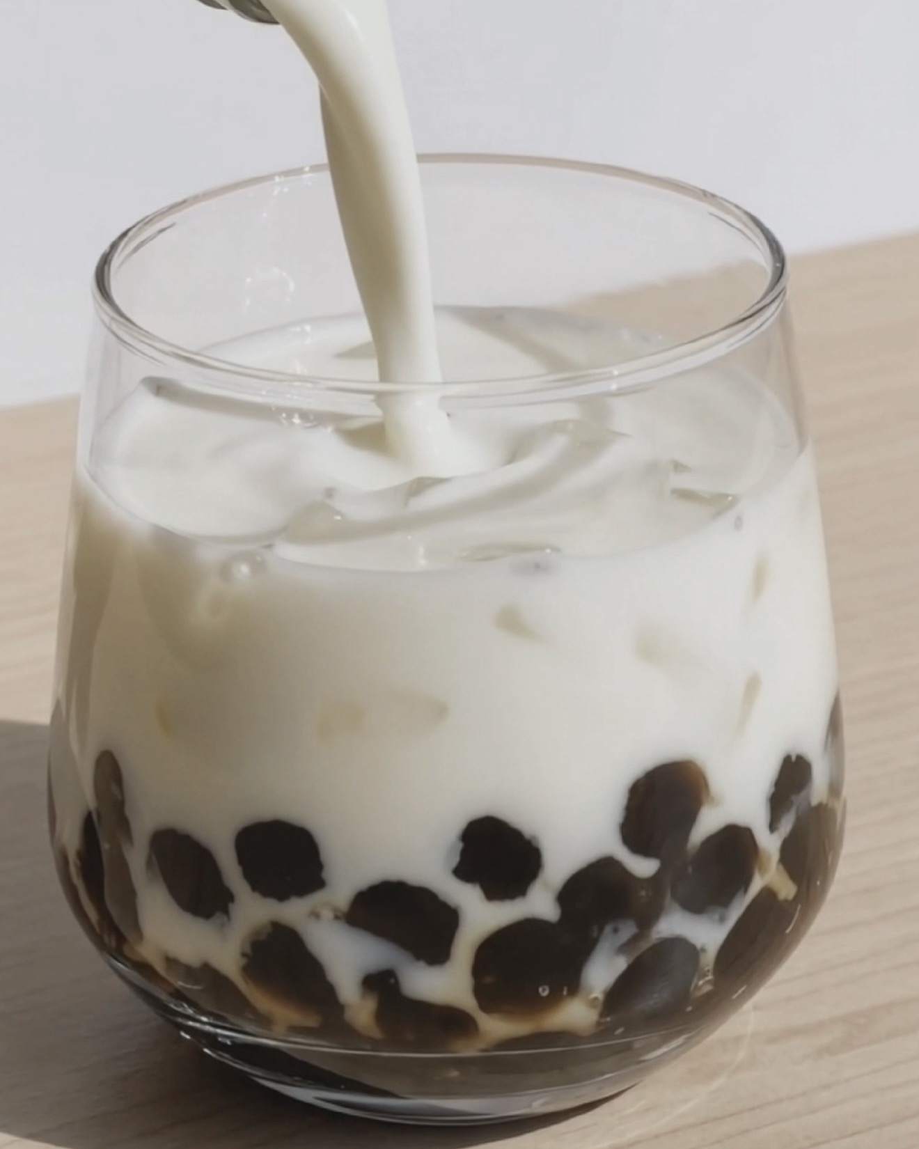 Tall glass with black tapioca pearls and brown sugar syrup streaks ready for the ube milk, by Ube Nolia