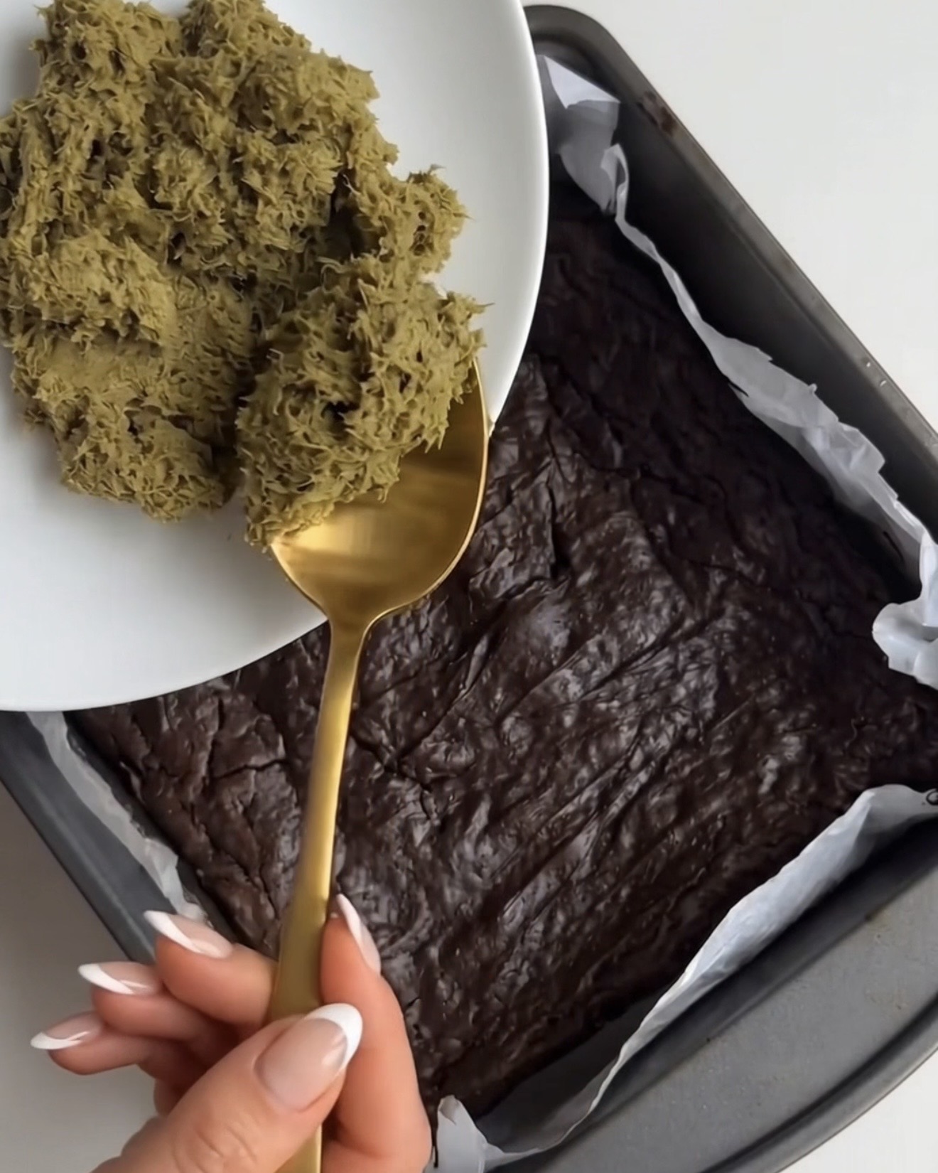 Pistachio kataifi filling being spooned onto the baked brownie base for Ube Dubai chocolate brownie bars by Ube Nolia