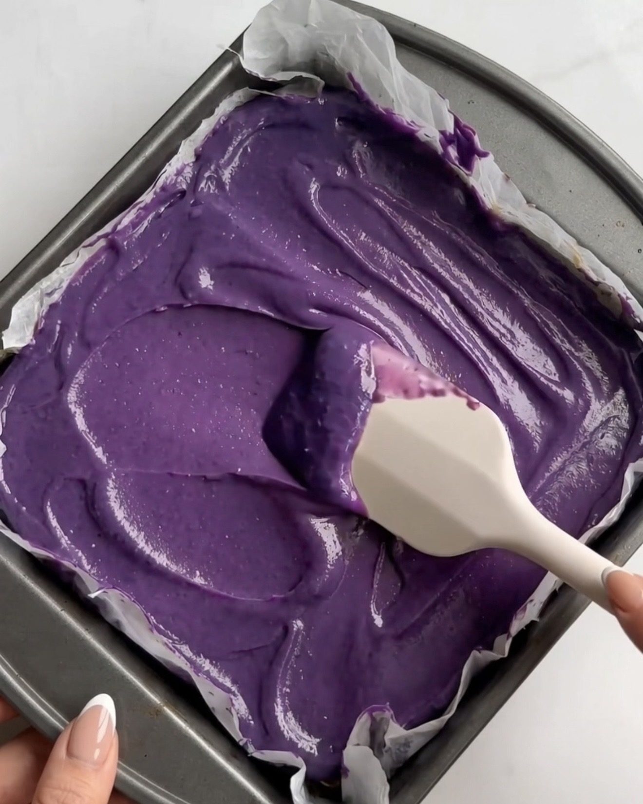 Vivid purple ube white chocolate ganache being spread over the pistachio kataifi layer for Ube Dubai chocolate brownie bars by Ube Nolia