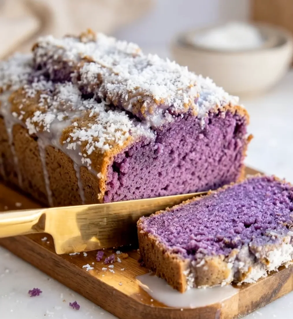 Sliced purple ube coconut loaf cake on a wooden board with white coconut topping and a gold knife, Ube Nolia recipe
