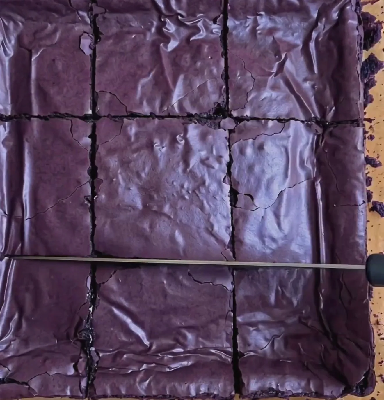 Baked gooey ube brownies with shiny deep purple crinkly top, sliced into 9 squares with Ube Nolia powder