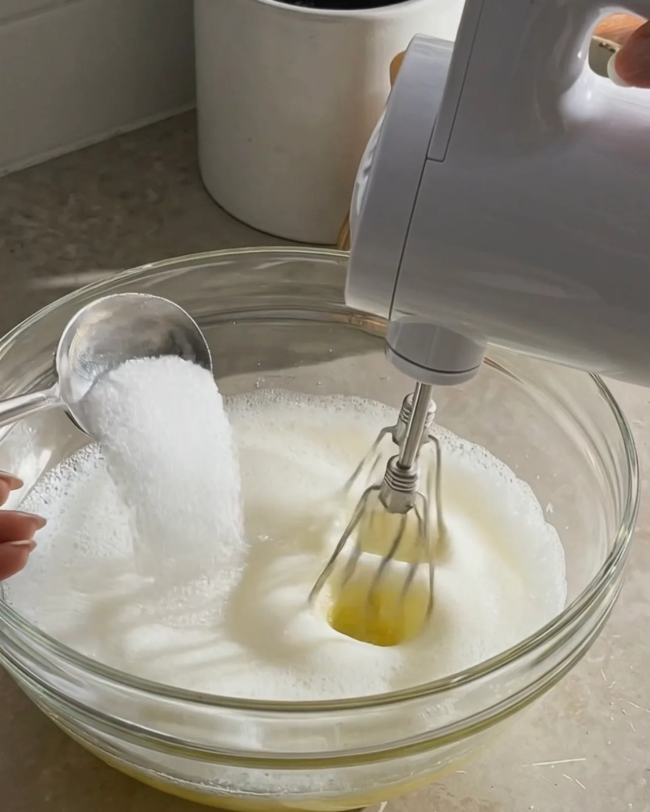 Adding sugar to foamy egg whites while whipping with an electric mixer for ube roll cake by Ube Nolia