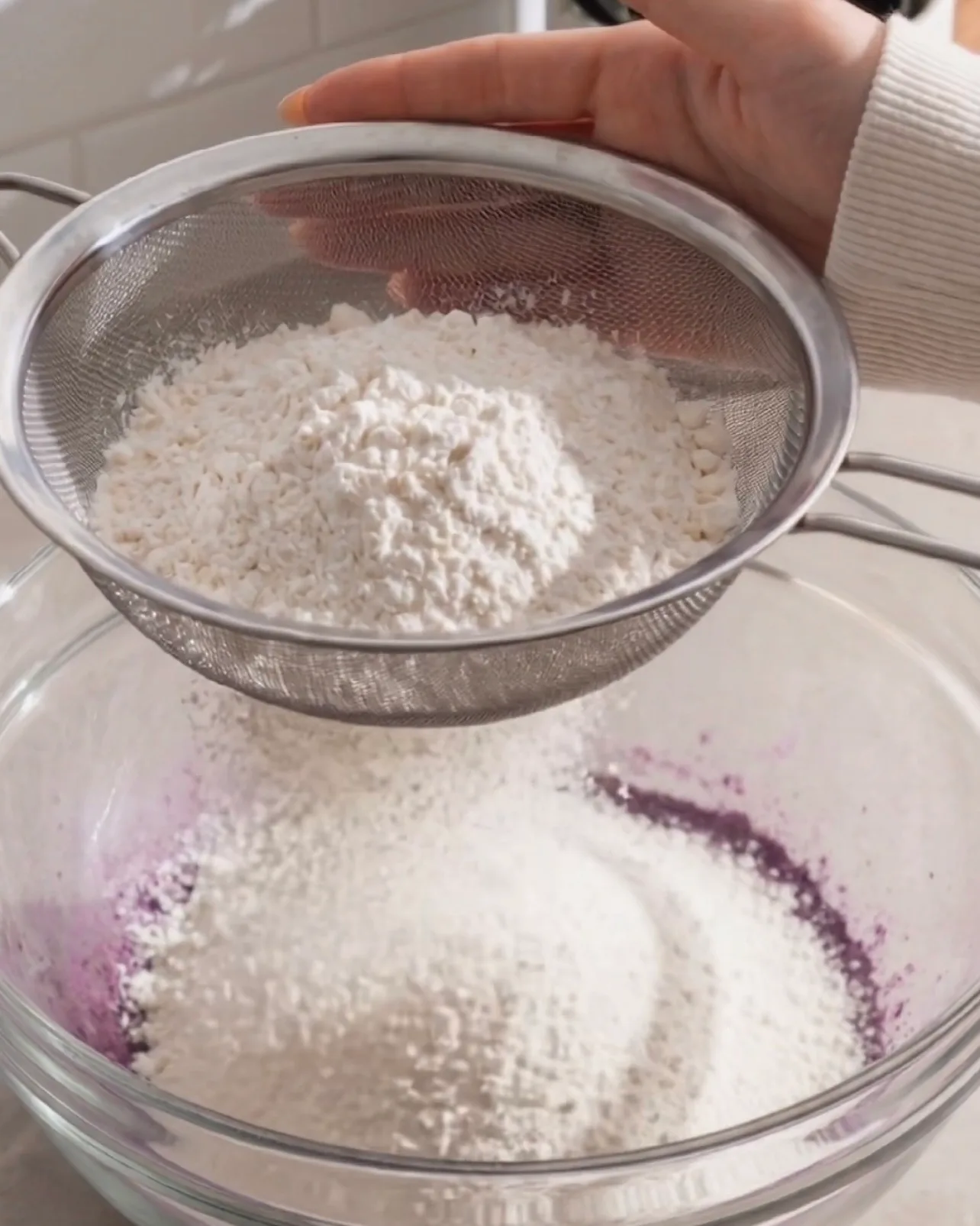 Sifting cake flour into purple ube batter through a fine mesh sieve by Ube Nolia