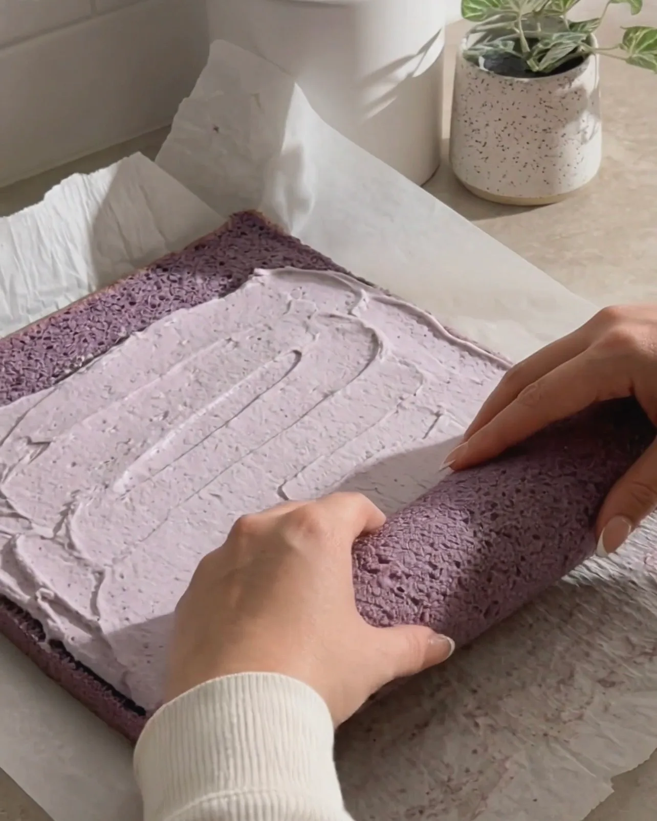Spreading ube whipped cream on the purple chiffon cake and rolling it up by Ube Nolia