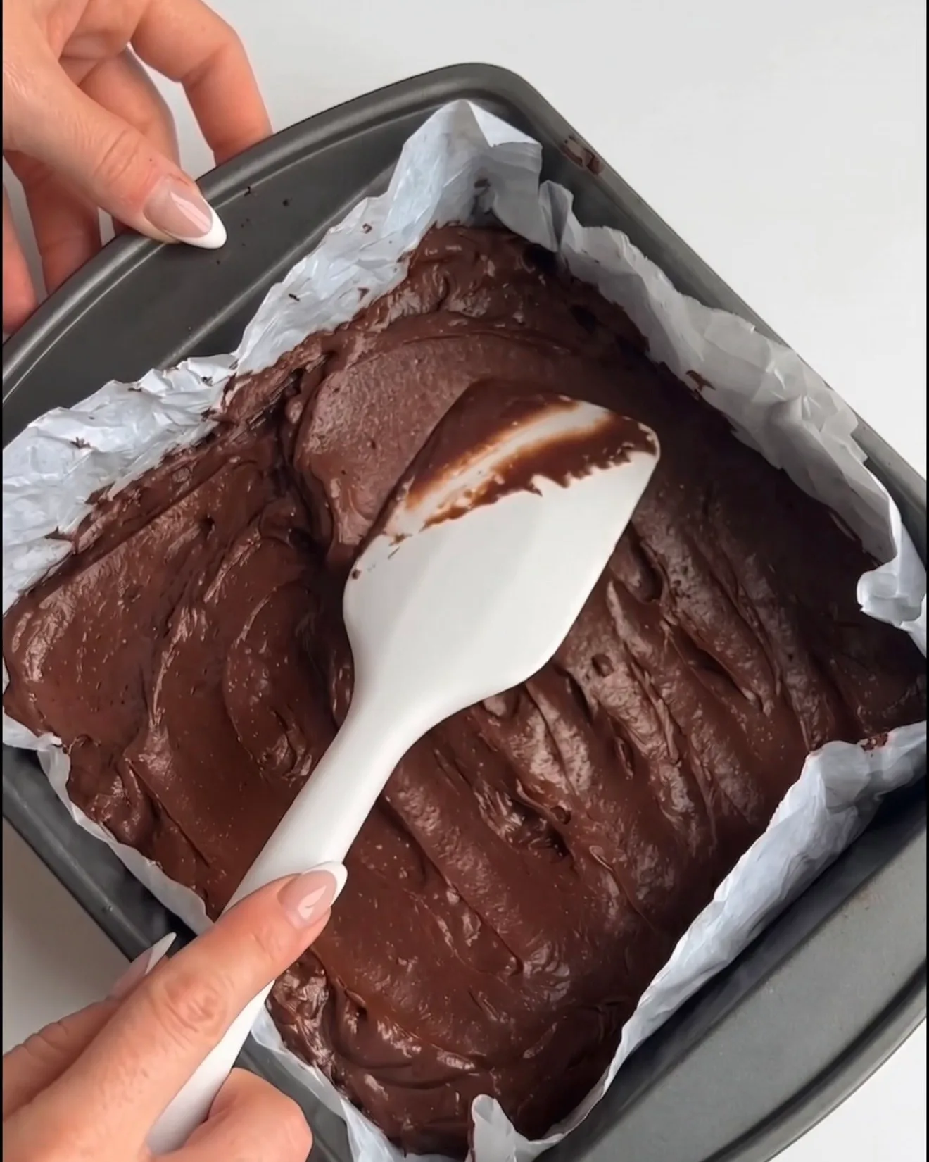 Slät Ube Dubai chokladbrownie-smet spridd i en bakplåtspappersklädd fyrkantig form, redo att bakas för Ube Nolia-receptet